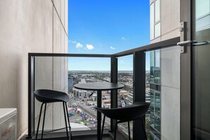 Een balkon met twee stoelen en een tafeltje, met uitzicht op een stadsgezicht met gebouwen en een weg.