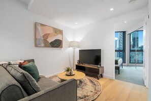 Een moderne woonkamer met een bank, een salontafel, een televisie en een schilderij aan de muur.
