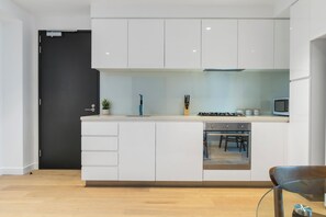 Een moderne keuken met witte kasten, een inbouwoven en een eethoek met een glazen tafel en stoelen.