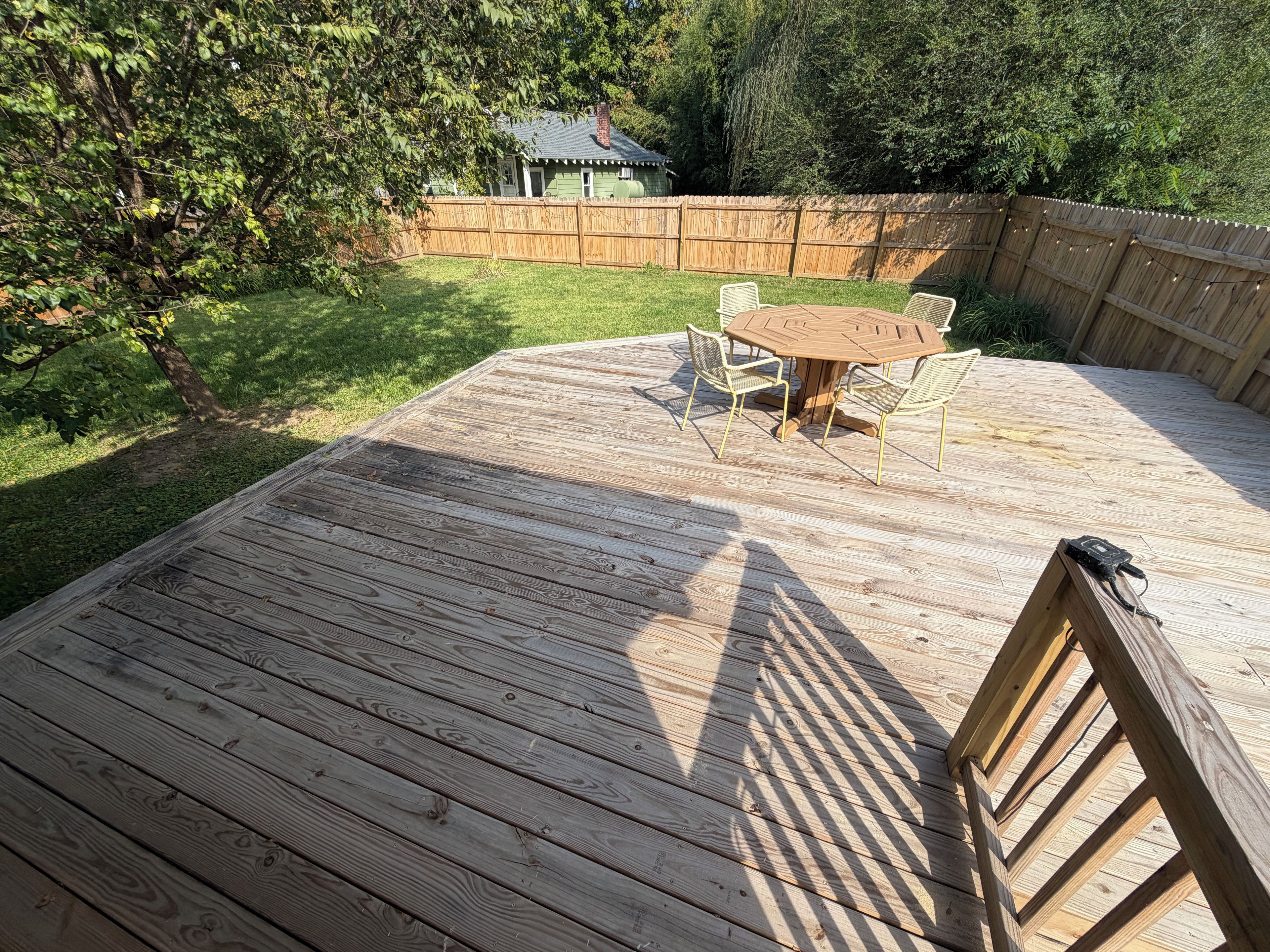 A wooden deck with a table and chairs, surrounded by a wooden fence and trees.