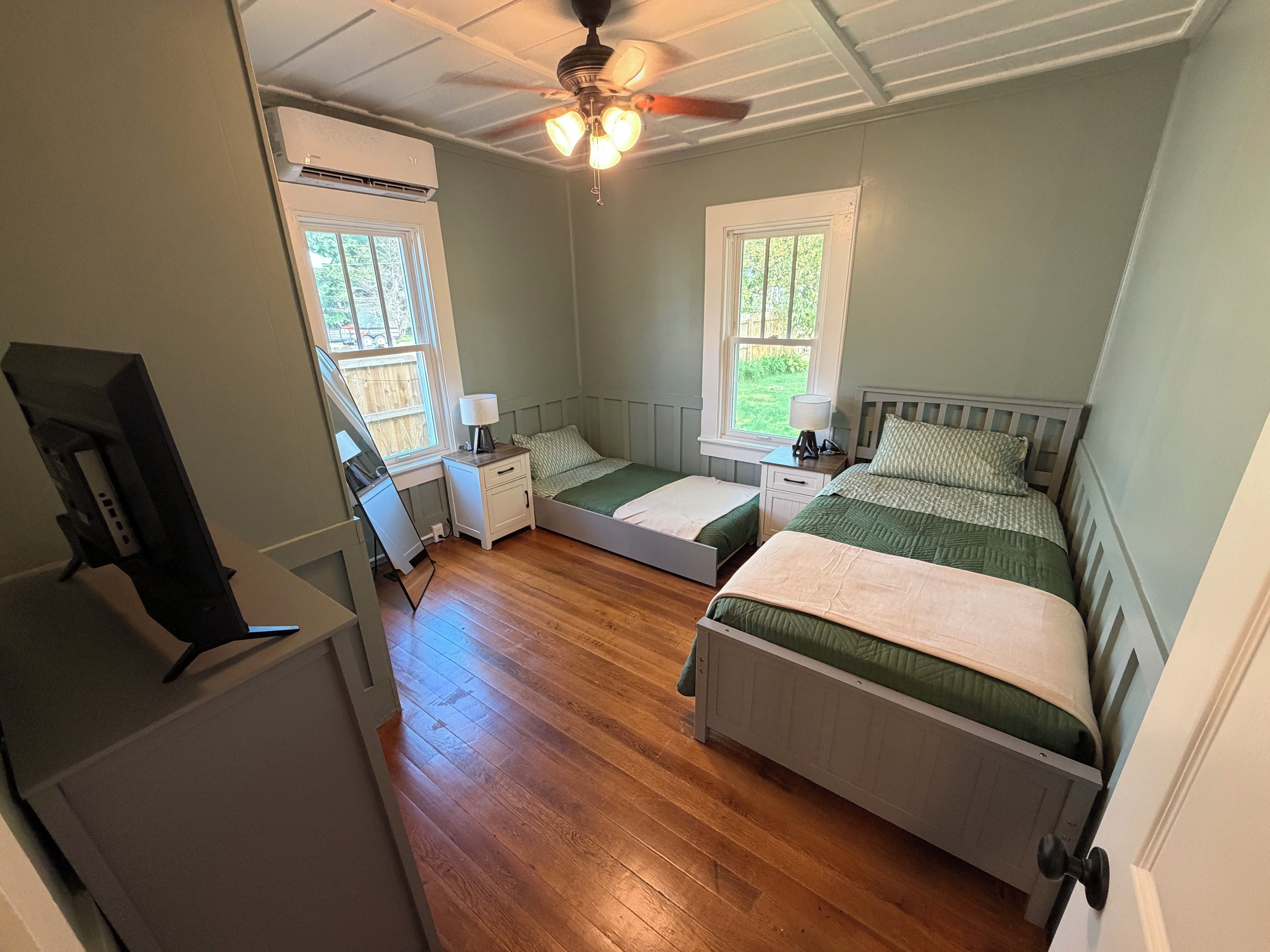 A bedroom with two beds, a desk, and a ceiling fan.