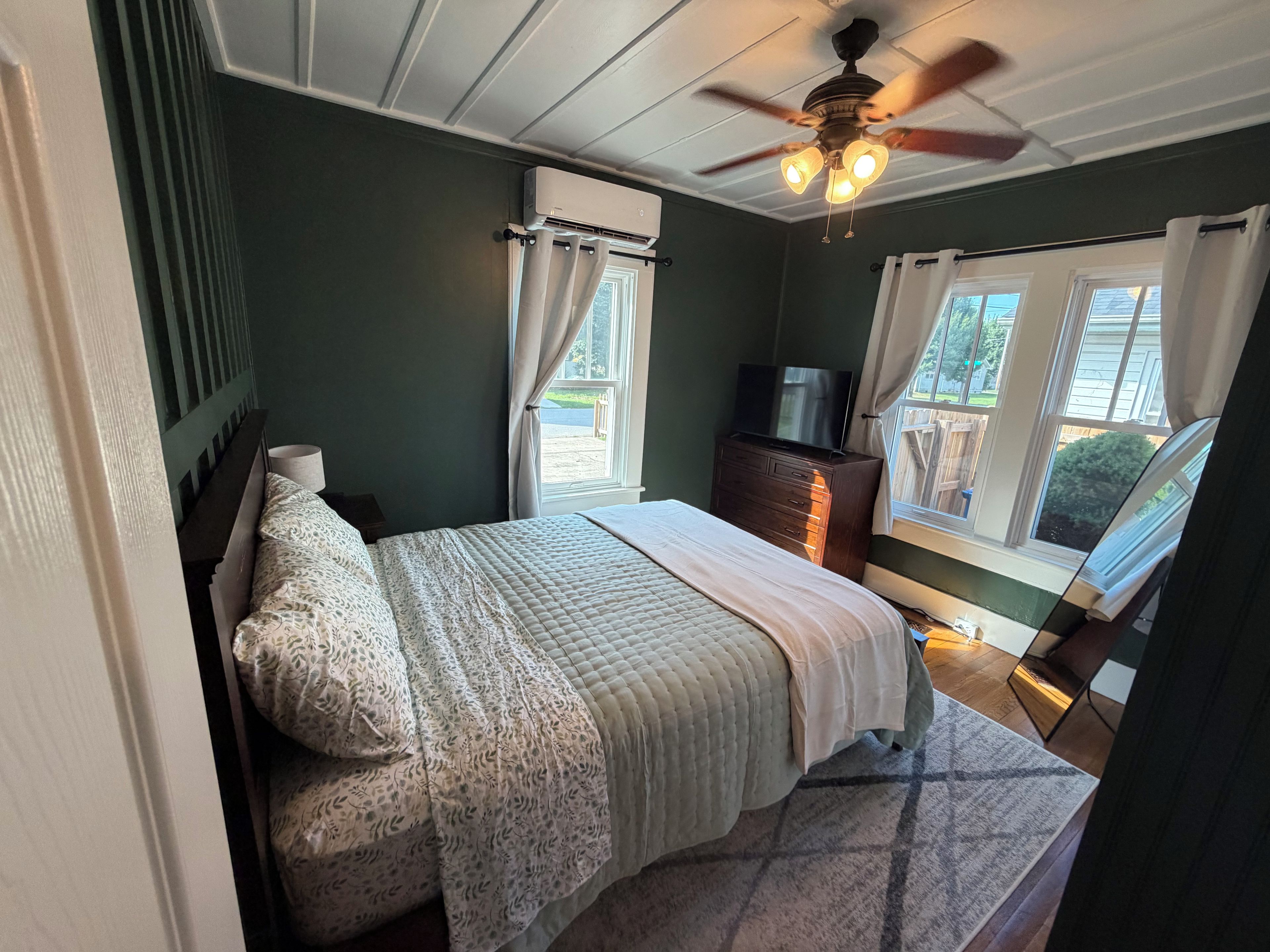 Un dormitorio con cama, cómoda, televisor y ventilador de techo.