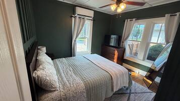 Un dormitorio con cama, cómoda, televisor y ventilador de techo.