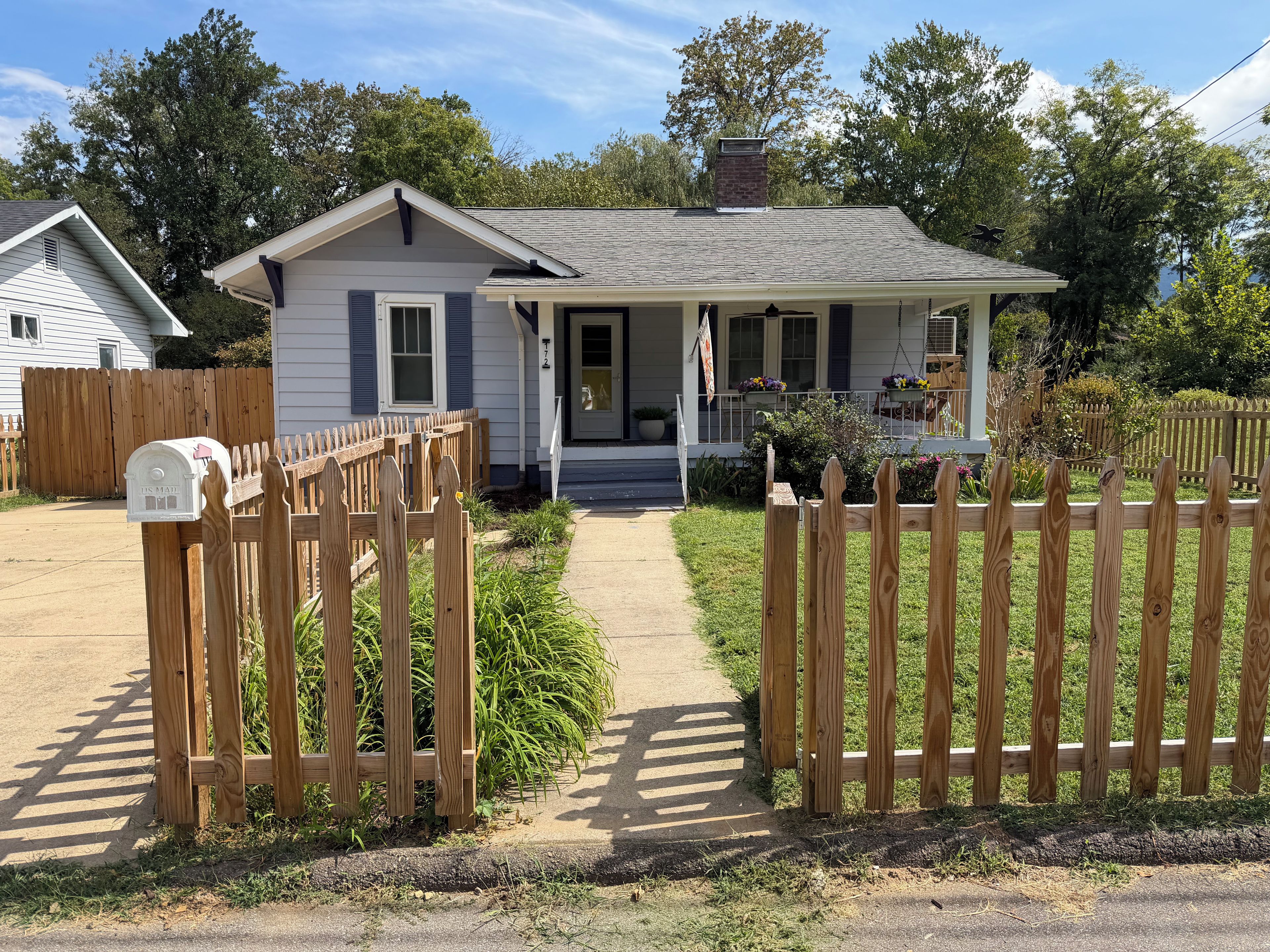 A single-story house with a front porch, a mailbox, and a wooden fence.