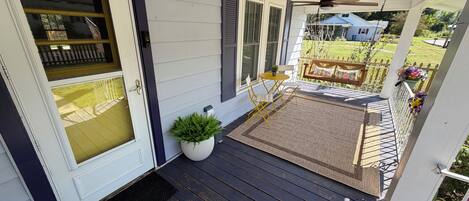 A porch with a wooden floor, a white door, and a small potted plant.