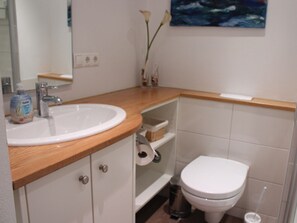 Ein Badezimmer mit einem weißen Waschbecken, einer Holzablage, einer weißen Toilette und einem Mülleimer.