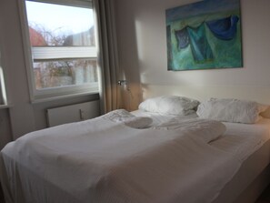 Ein ordentlich bezogenes Bett mit weißen Leinen in einem Zimmer mit Fenster und einem Bild an der Wand.