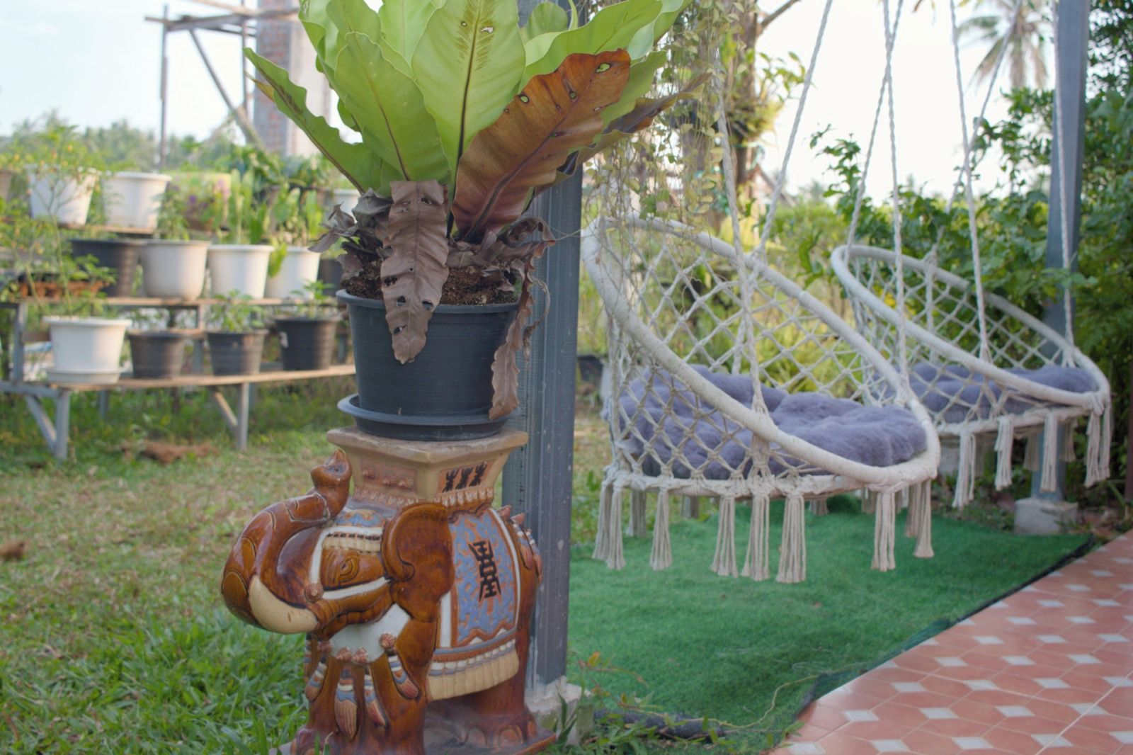 Een tuin met een plant in een pot, een decoratieve keramieken olifant en een hangstoel.