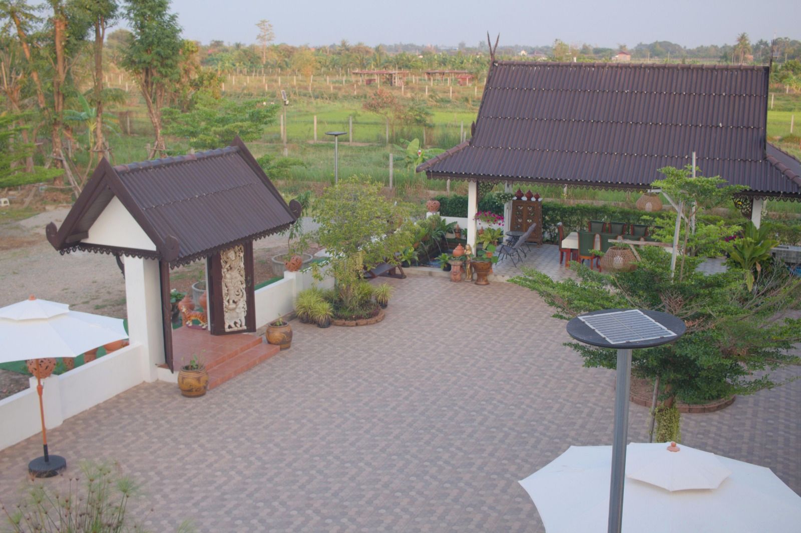 A courtyard with traditional-style pavilions, a paved walkway, and a variety of potted plants.