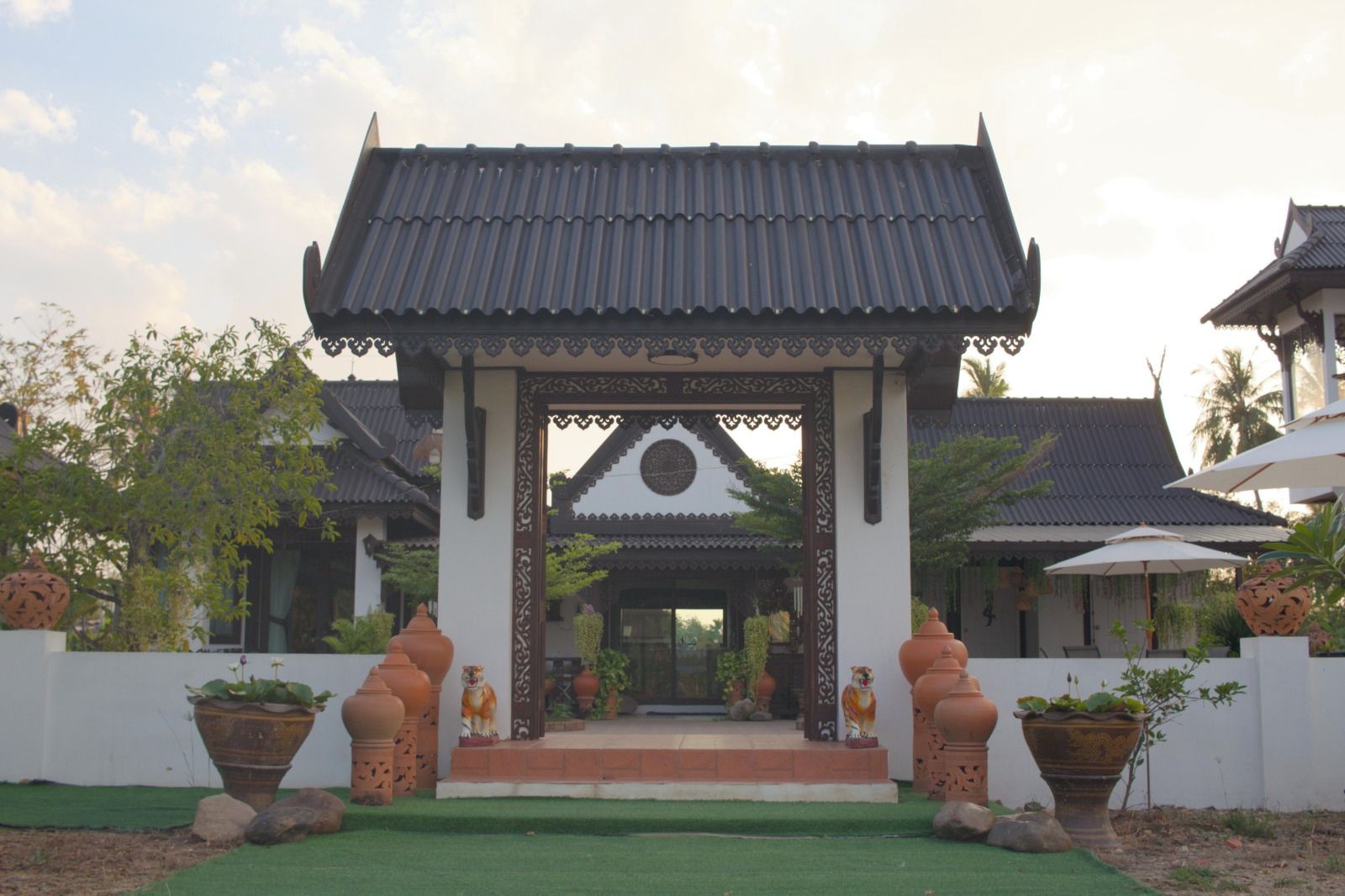A traditional architectural structure with a tiled roof, a central entrance with decorative elements, and potted plants.