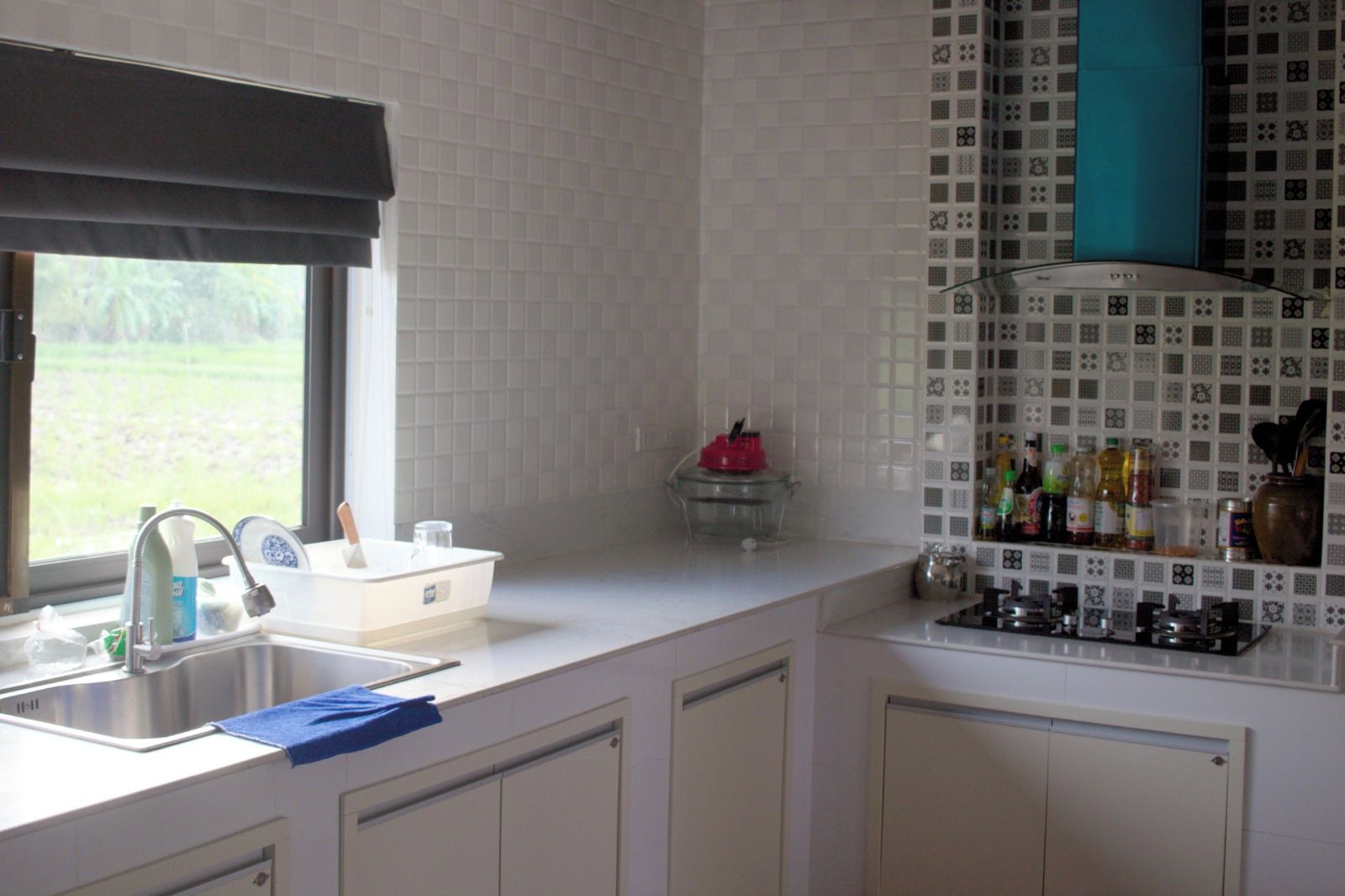 Een keuken met een raam, een spoelbak, kastjes en een betegelde spatwand.
