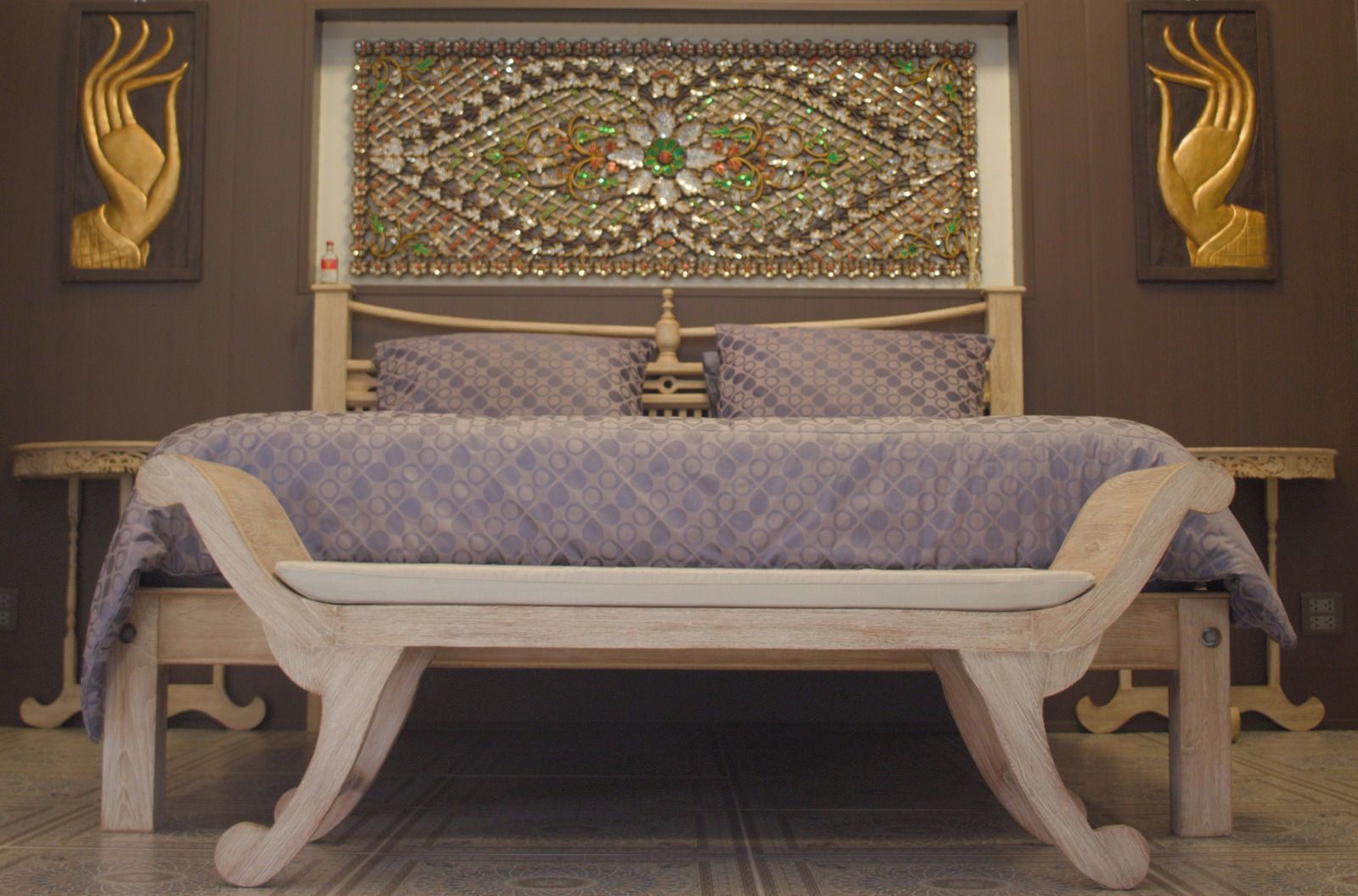Un lit avec une couvre-lit à motifs, une tête de lit décorative et un banc en bois placé devant.
