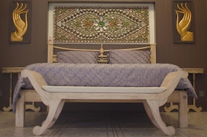 Una cama con una colcha estampada, un cabecero decorativo y un banco de madera al frente.