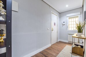 Ein Flur mit einer weißen Tür, einem Heizkörper, einem Fenster mit Jalousien und einer Pflanze auf einem Regal.