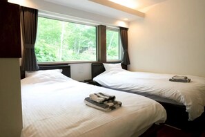 Ein Hotelzimmer mit zwei Betten, einem Fenster mit Vorhängen und Blick auf Grünfläche.