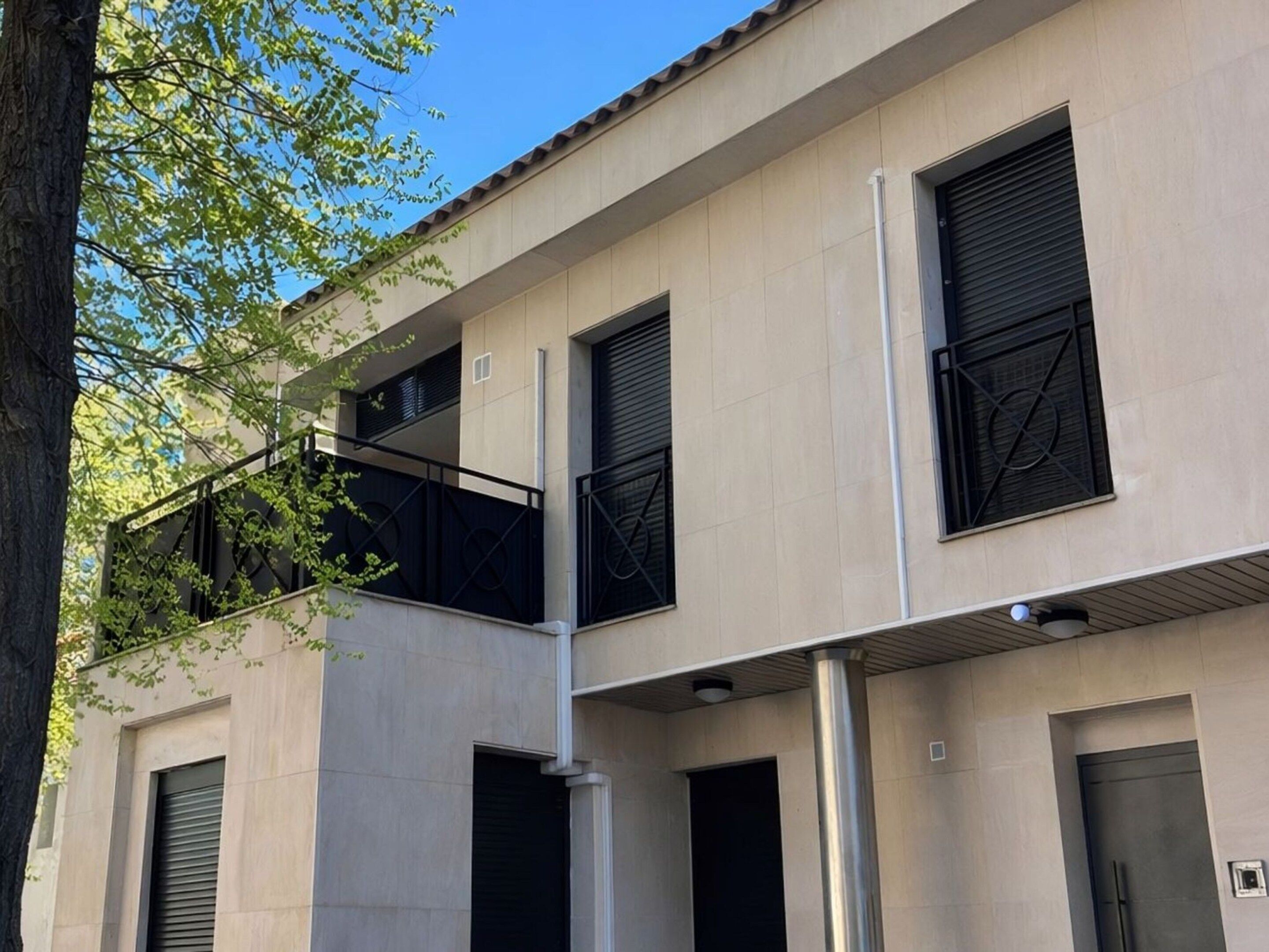 Un edificio de varios pisos con fachada plana, ventanas amplias con contraventanas y un balcón con barandillas de metal.