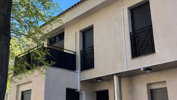 Un edificio de varios pisos con fachada plana, ventanas amplias con contraventanas y un balcón con barandillas de metal.
