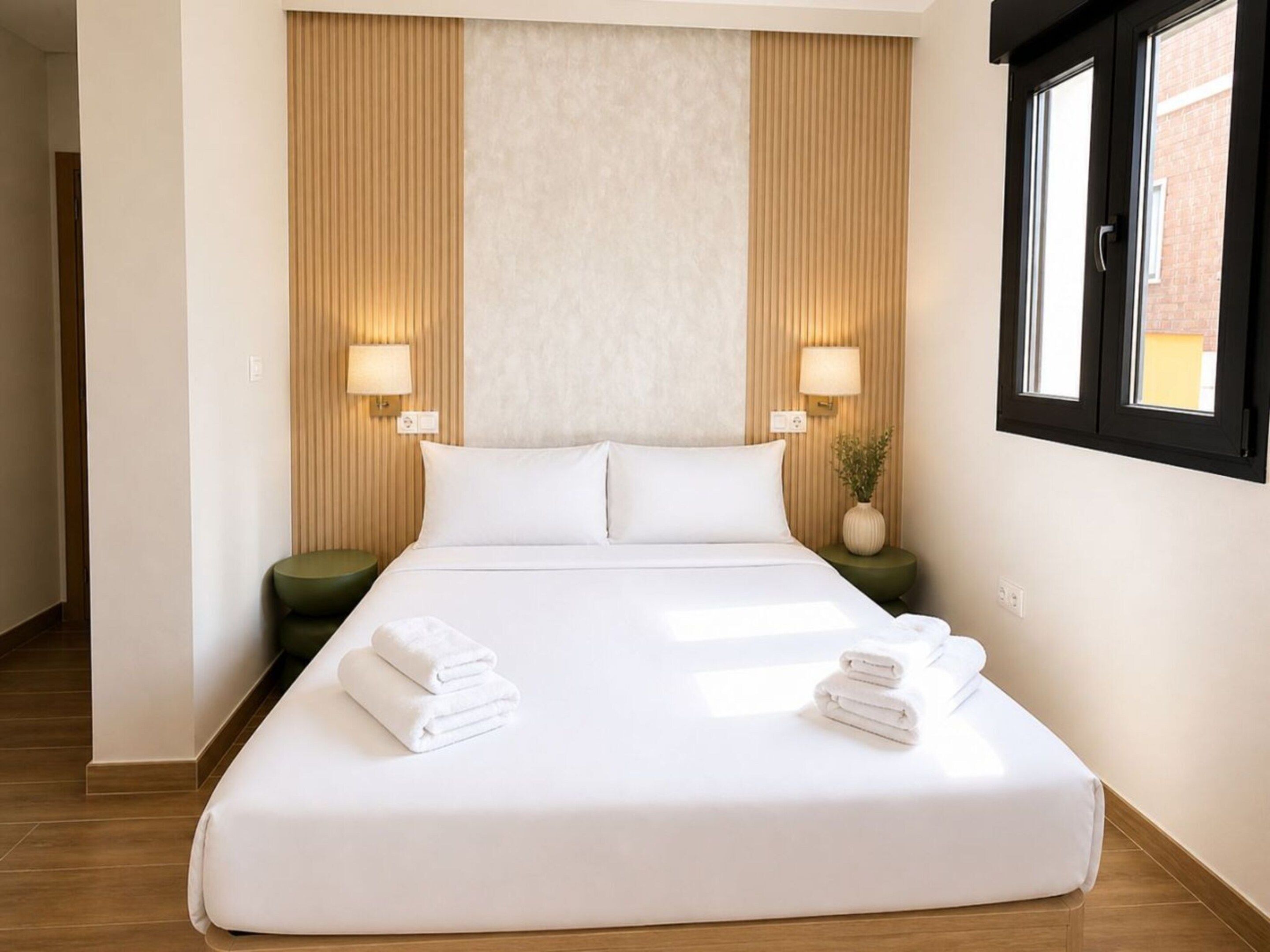 Una habitación de hotel con una cama grande, dos lámparas de noche, una mesita de noche verde y una ventana con persianas.
