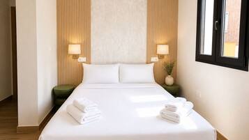 Una habitación de hotel con una cama grande, dos lámparas de noche, una mesita de noche verde y una ventana con persianas.