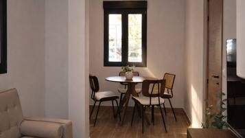 Un pequeño comedor con una mesa redonda y cuatro sillas, una ventana con persianas, y un sofá al frente.