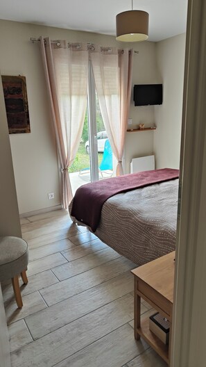 A bedroom with a bed, a bedside table, a television on the wall, and a window with curtains. - Charming single-family home, 70 m2, on enclosed property, in a completely quiet setting (Saint-André-les-Alpes)