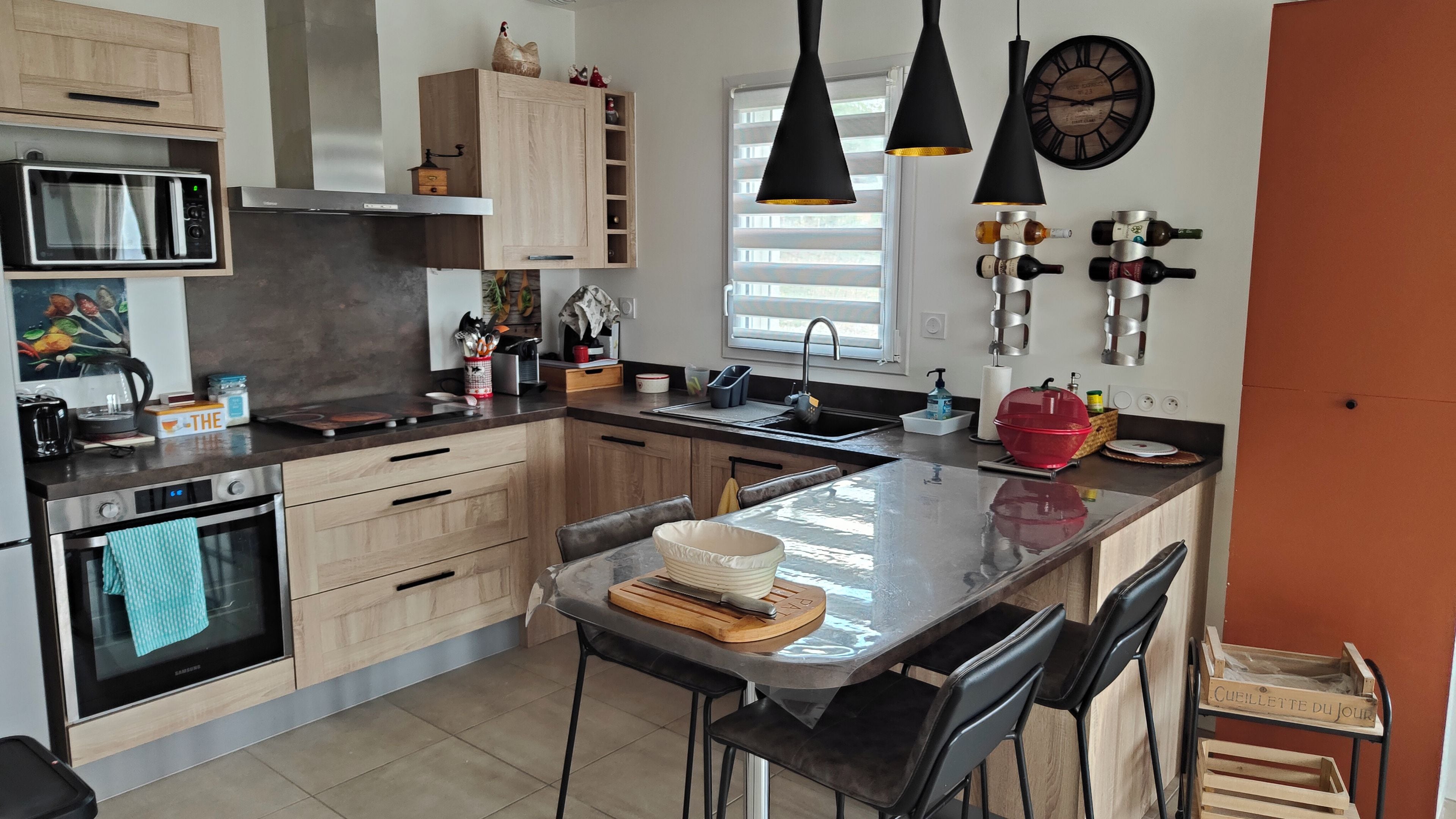 Una cocina moderna con una isla central, electrodomésticos de acero inoxidable y una ventana con persianas.