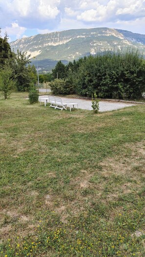 Eine grüne Wiese mit einer Bank, Bäumen und einem Berg im Hintergrund.