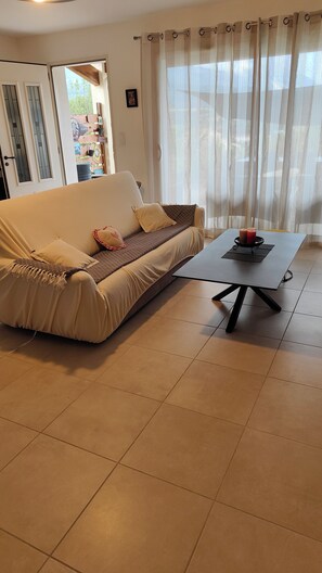 Ein Wohnzimmer mit einer Couch, einem Couchtisch und Blick durch leichte Vorhänge.