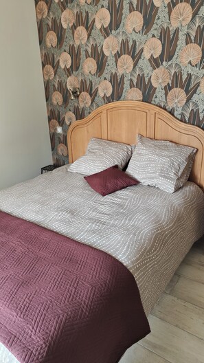 Ein Bett mit einem gemusterten Bettüberwurf, zwei Kissen und einer roten Tagesdecke.