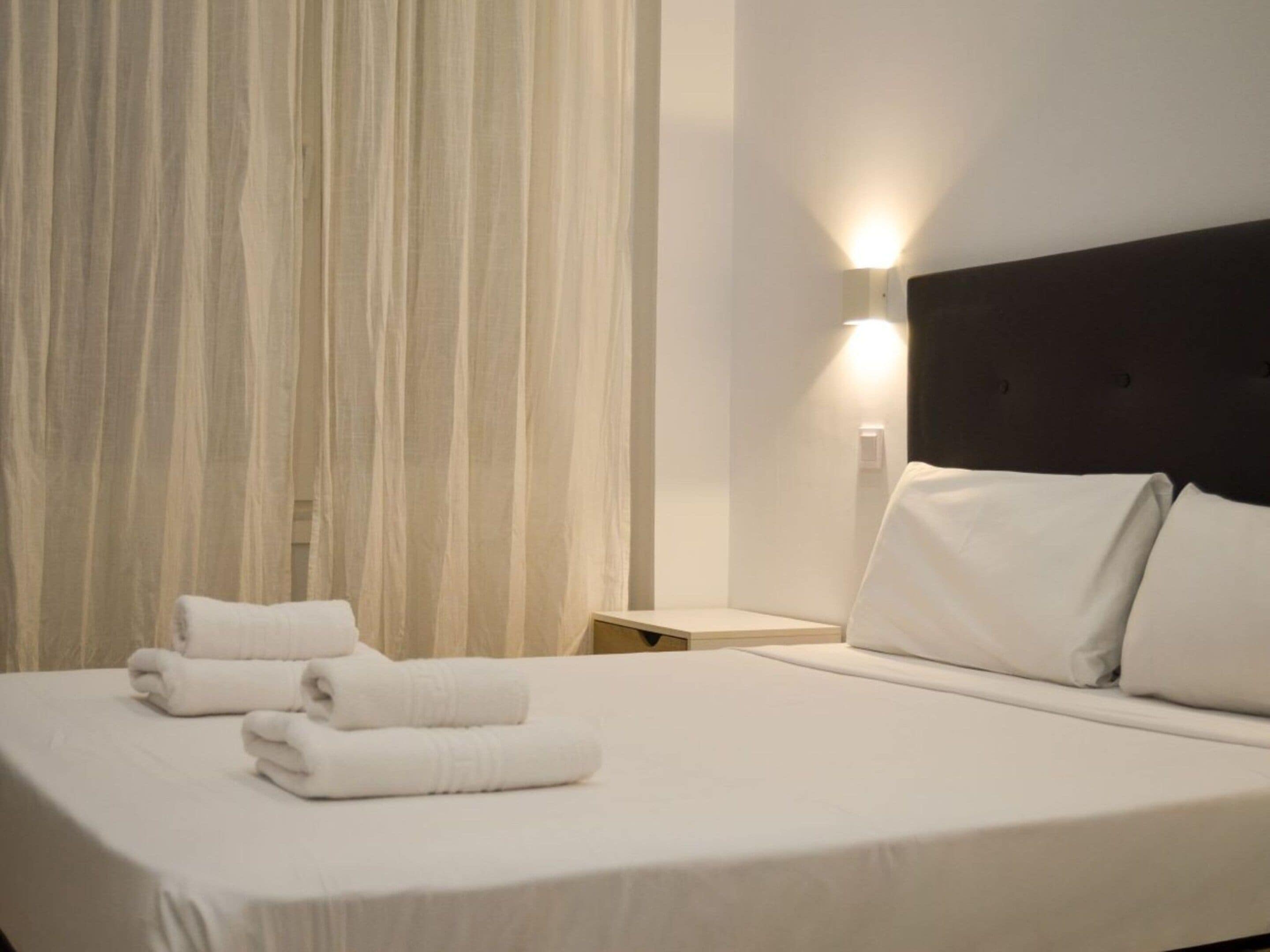 Una habitación de hotel con una cama bien hecha, una mesita de noche y una lámpara de pared.