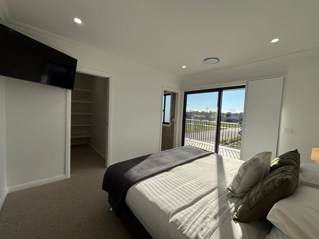 A bedroom with a large bed, a closet, and a sliding glass door leading to a balcony.