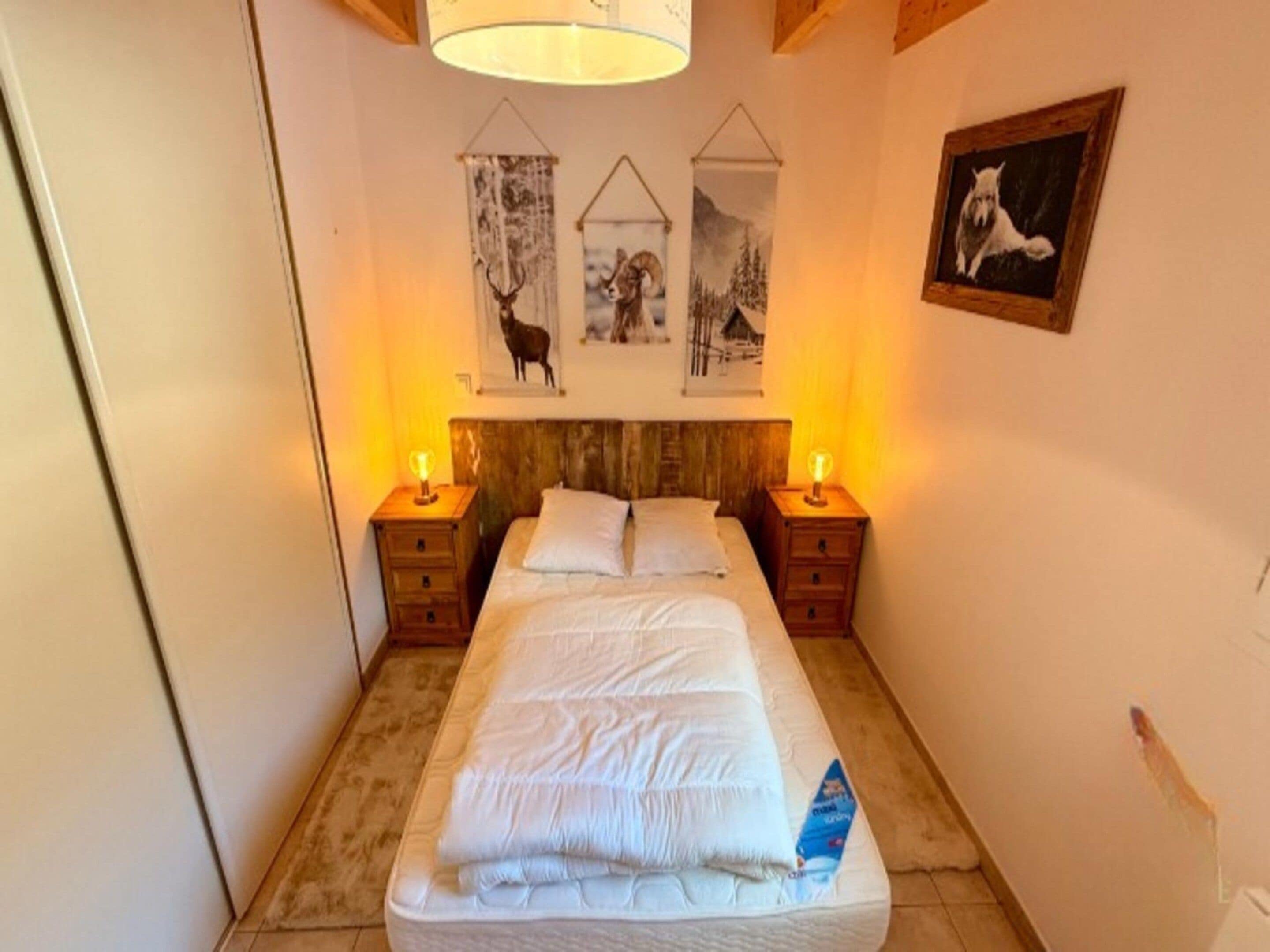 A bedroom with a bed, two bedside tables with lamps, a headboard, and three wall-mounted pictures.