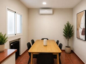 A conference room with a wooden table, black chairs, a white air conditioning unit, a radiator, and two potted plants. - Spacious Madrid Apartment With Garden (Madrid)