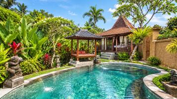Una piscina cristalina con un pabellón y escalones que conducen a un área techada, rodeada de exuberante vegetación y plantas tropicales.