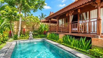 A pool with a stone statue, surrounded by lush greenery and a wooden building with a balcony.