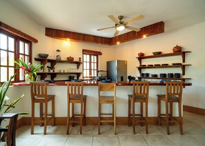 A kitchen with wooden chairs, a ceiling fan, and shelves with dishes. - Spacious 3BR, 3.5BA home just minutes from Playa Maderas (San Juan del Sur)