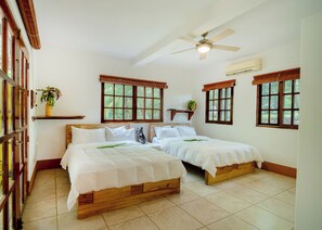 Une chambre d’hôtel avec deux lits en bois, un ventilateur de plafond et de grandes fenêtres avec des cadres en bois.