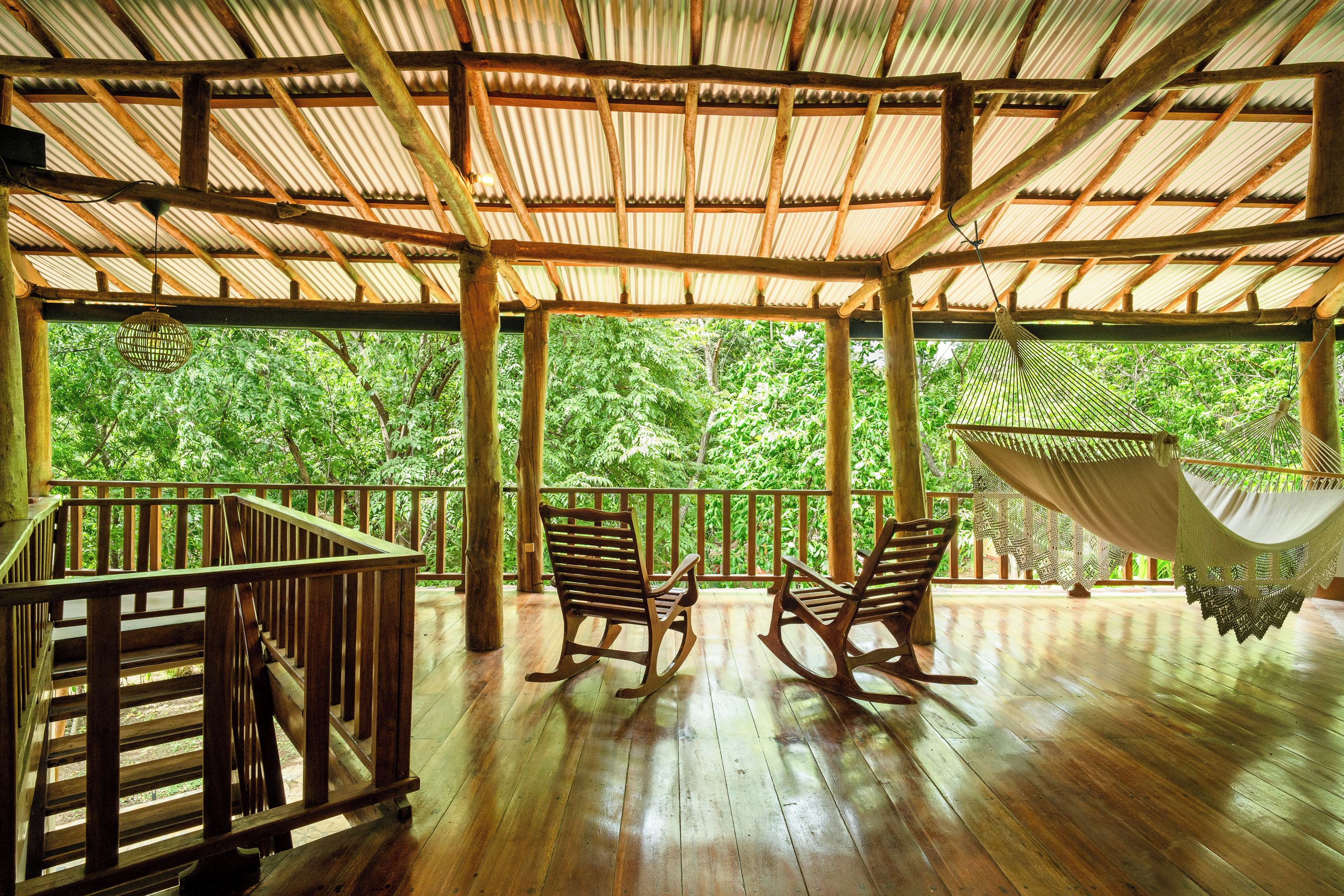 Une terrasse en bois surmontée d’un toit de chaume, avec des fauteuils à bascule en bois et un hamac.