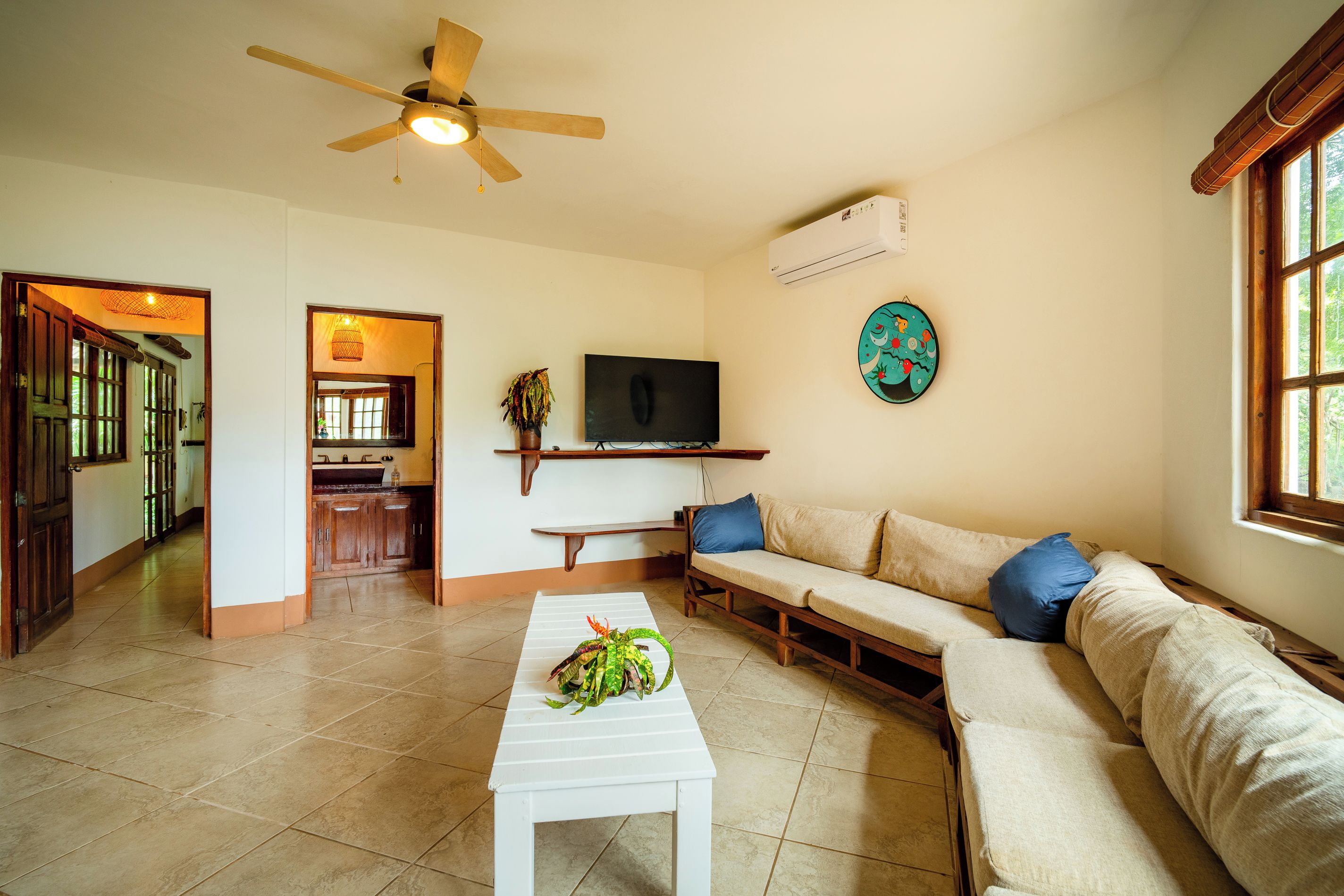 A living room with a ceiling fan, a television, a sofa, and a dining area with a window.