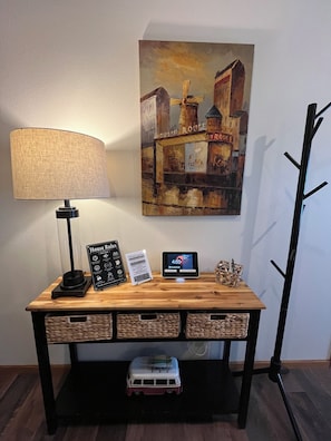Un escritorio de madera con una lámpara, un reloj digital, un cartel de bienvenida y un cartel con las normas de la casa.