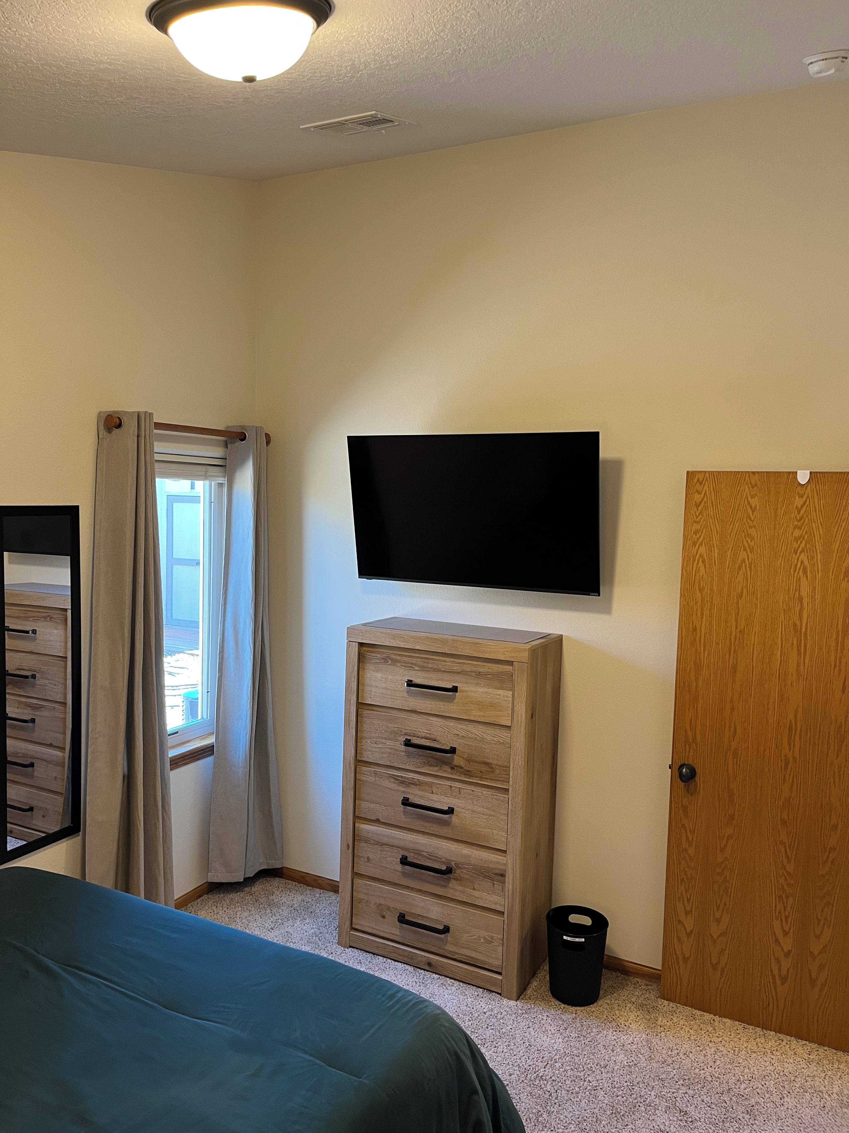 Een slaapkamer met een bed, een dressoir, een aan de muur bevestigde televisie en een deur.