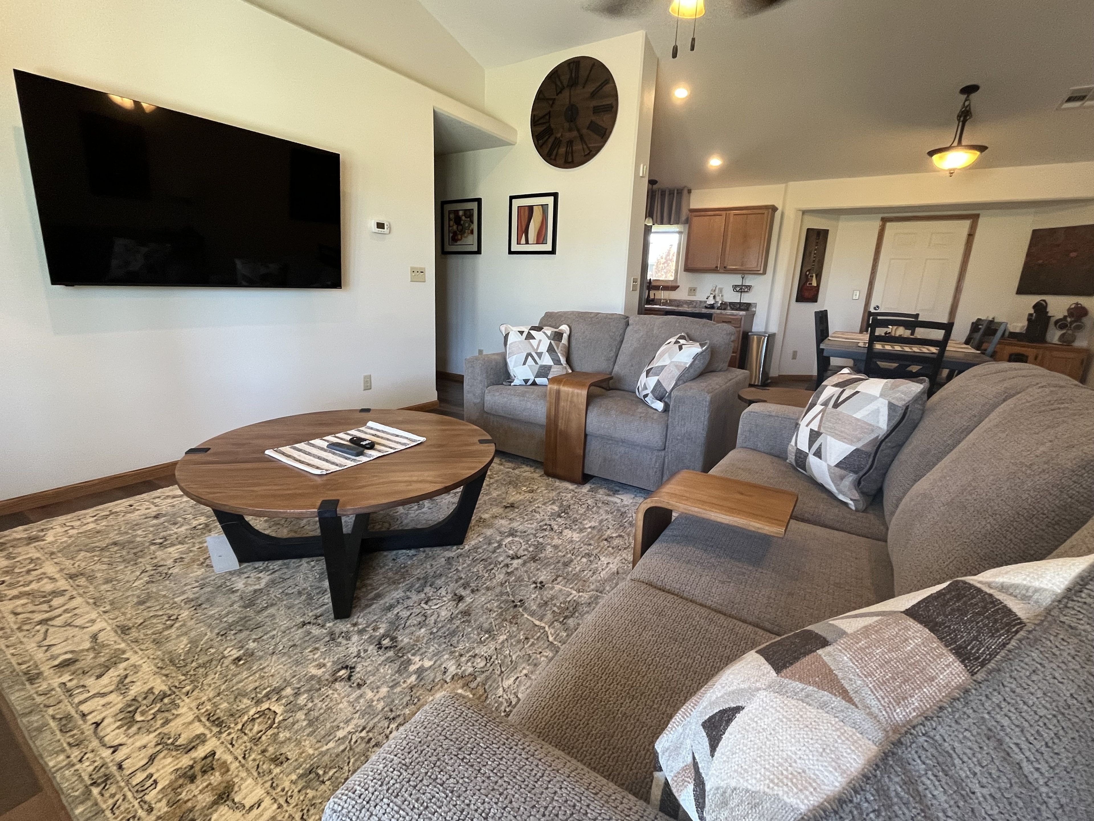 A living room with a flat-screen TV, a round coffee table, and two sofas with patterned throw pillows.