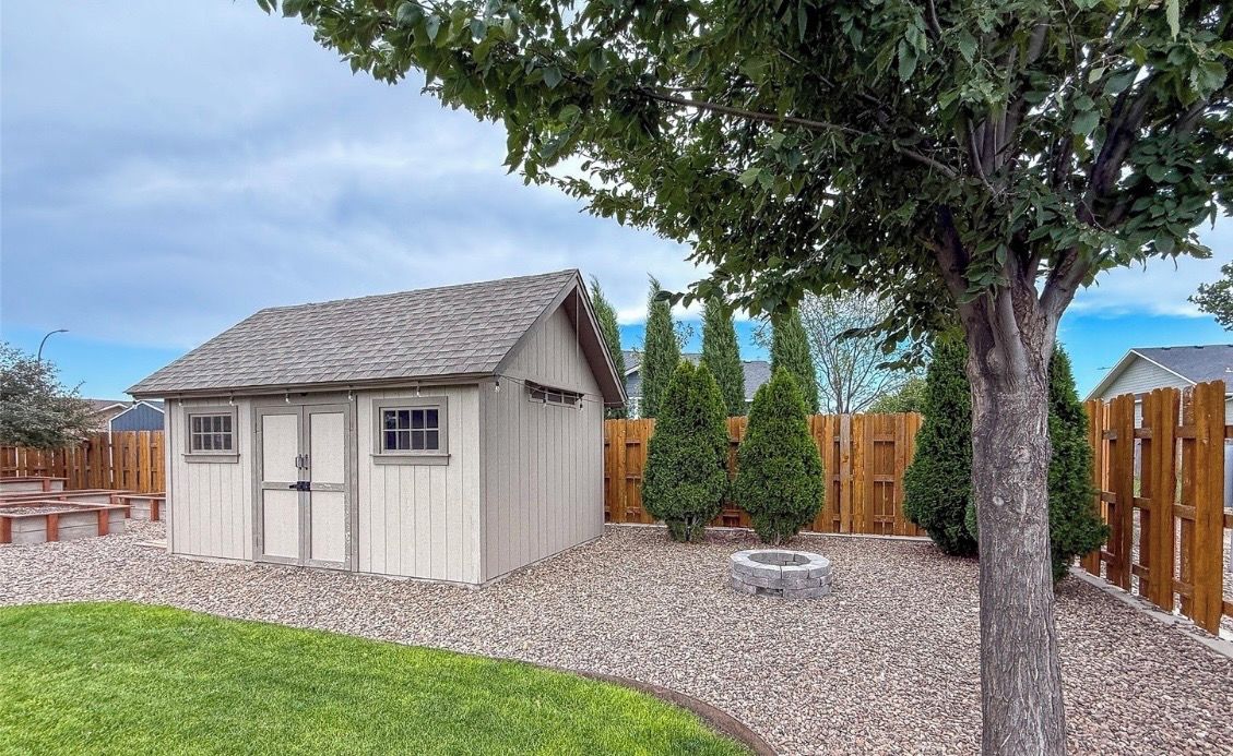 A small wooden shed with a sloped roof, a gravel driveway, and a wooden fence in the background.