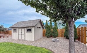 A small wooden shed with a sloped roof, a gravel driveway, and a wooden fence in the background.