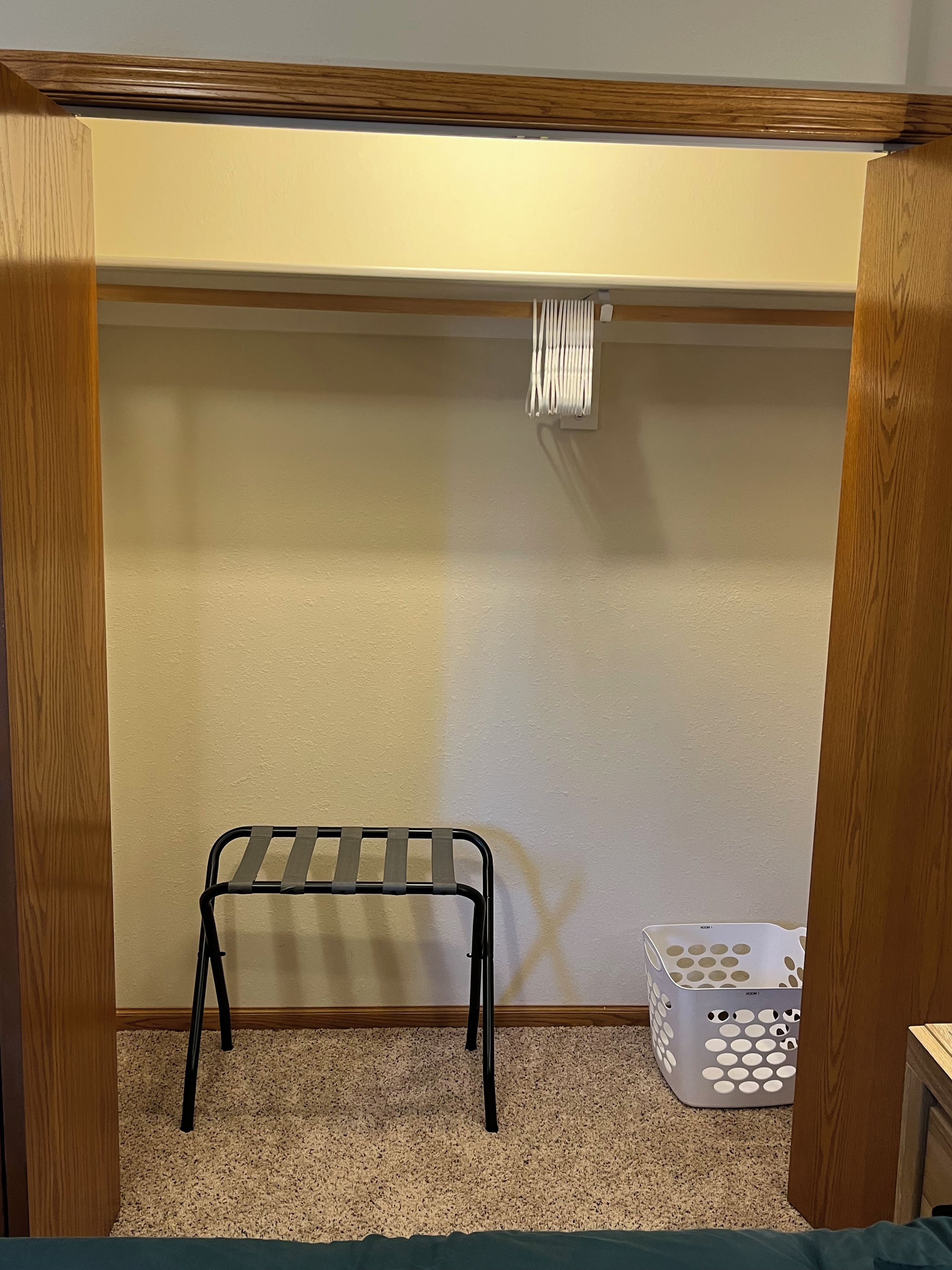 Un petit placard fermé, avec une étagère en métal, un panier à linge blanc et un cadre de porte en bois.