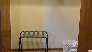 Un petit placard fermé, avec une étagère en métal, un panier à linge blanc et un cadre de porte en bois.