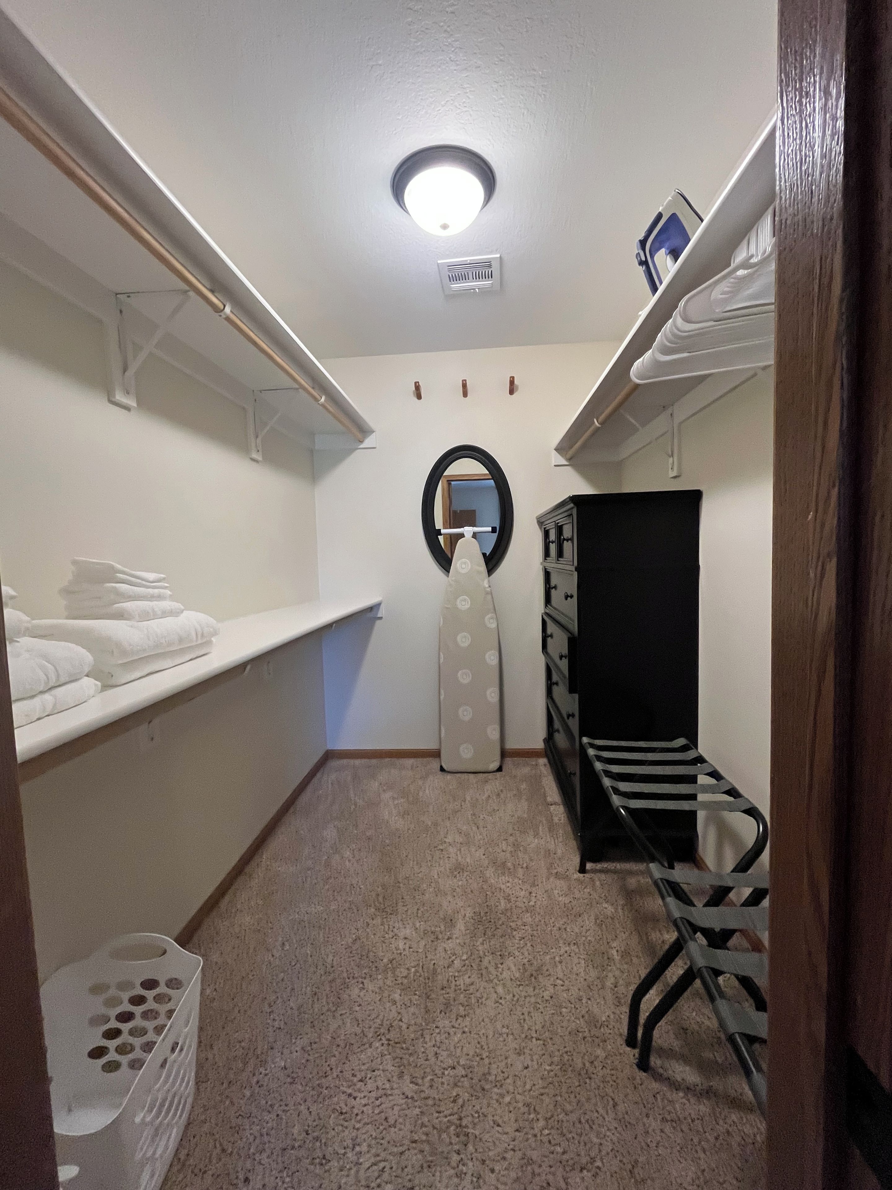 A laundry room with shelves for folded towels, a drying rack, a wall-mounted mirror, and a vent.