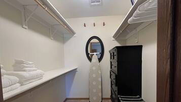 A laundry room with shelves for folded towels, a drying rack, a wall-mounted mirror, and a vent.