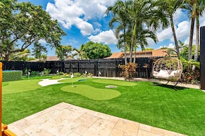 A backyard with a putting green, palm trees, and a hanging chair. - Heated pool, hot tub, sauna, golf, theater, lounge (West Palm Beach)