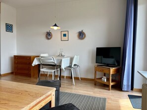 A living room with a dining area, a TV, and a wooden cabinet. - Berliner Ring - Apt. 27 (Wyk auf Foehr)